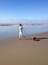 Woman walking with dog on sand against sea at beach