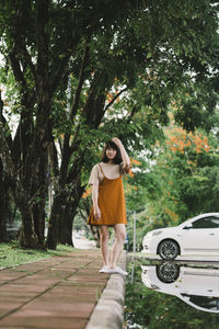 Full length of thoughtful woman standing on sidewalk by puddle