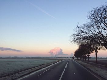 Road by trees against sky during sunset