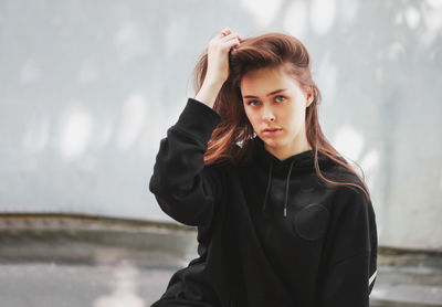 Portrait of beautiful young woman with hand in hair against wall