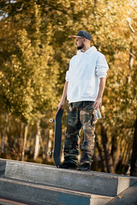 Full length of man standing by tree with skateboard