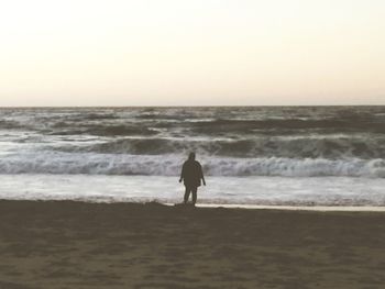 Rear view of silhouette man on beach against clear sky
