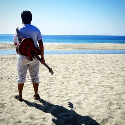 Rear view of man playing on beach against clear sky