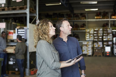 Mature colleagues looking away while holding digital tablet at warehouse