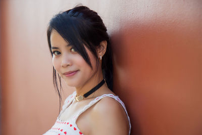 Asian woman in a white dress with heart patterned looking at the camera next to an orange wall