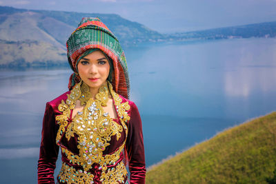 Portrait of beautiful woman wearing traditional clothing while standing on mountain against lake