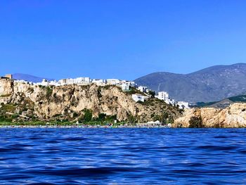 Scenic view of sea and mountains against clear blue sky