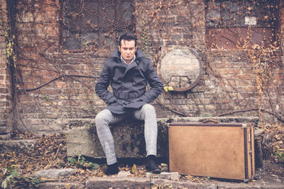 Portrait of young man sitting against brick wall