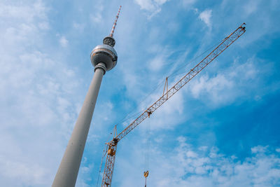 Low angle view of television tower and crane against cloudy sky