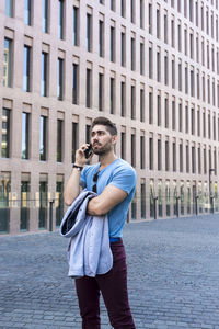 Handsome man talking over mobile phone while standing in city