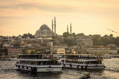 Boats moored in river by buildings against sky