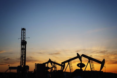 Silhouette oil pumps on field against sky during sunset