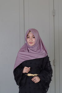 Portrait of a smiling young woman standing against wall