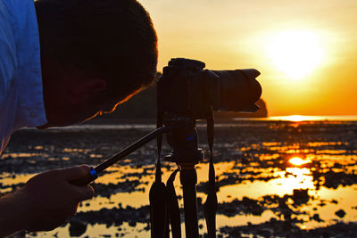 Photographer photographing at beach against sky during sunset