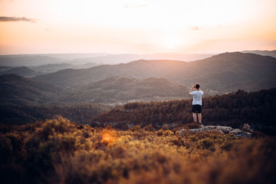 Rear view of man standing on mountain during sunset