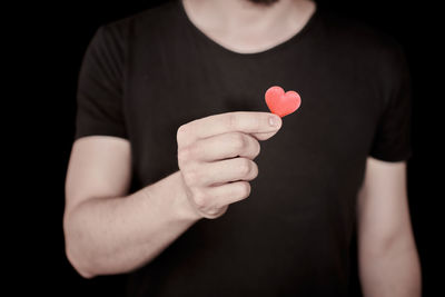 Midsection of man holding heart shape against black background