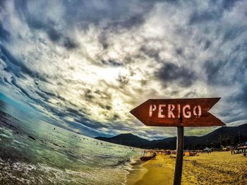 Road sign by water against sky