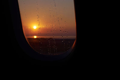 Close-up of wet glass window against sky during sunset