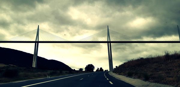 Low angle view of bridge over road against cloudy sky