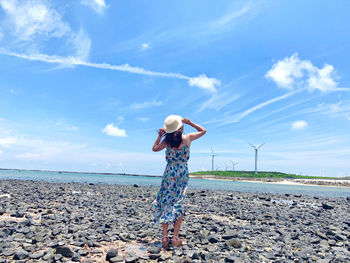 Rear view of woman standing at beach against sky