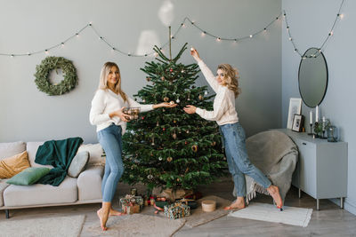 Two beautiful blonde sisters. having fun, getting ready for celebration, decorating christmas tree