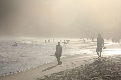 People walking on beach against sky during winter