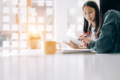Young woman using phone while sitting on table