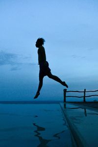 Side view of silhouette man jumping in sea against sky