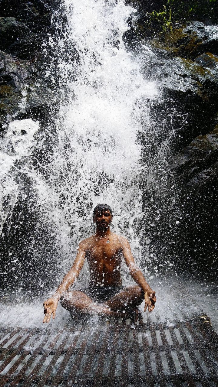 FULL LENGTH OF SHIRTLESS MAN SPLASHING WATER IN RAIN