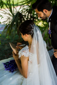 Groom looking at bride while writing on shoe during wedding ceremony