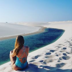 Rear view of woman sitting on sand by river