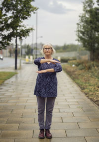 Full length portrait of woman gesturing while standing on footpath against buildings