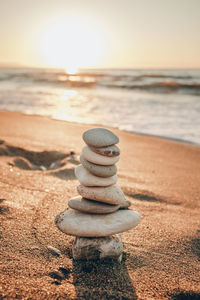 Stack of pebbles on beach against sky during sunset