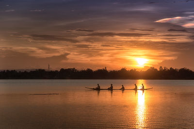 Side view of silhouette people rowing rowboat in lake against sky during sunset