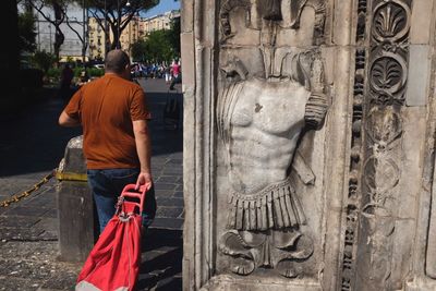 Rear view of man with luggage walking by carved wall