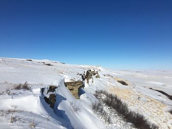 Snow covered landscape against clear blue sky