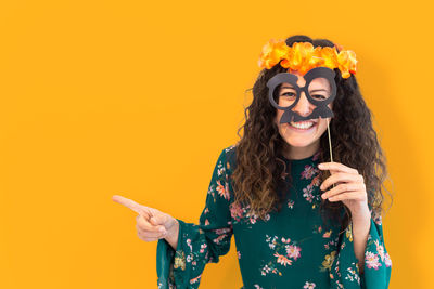 Portrait of smiling young woman holding umbrella against orange background
