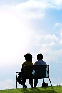 Rear view of man sitting on bench against sky