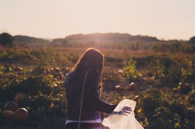 Rear view of woman holding plastic bag while standing on pumpkin field 
