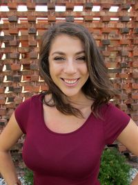 Portrait of smiling woman standing against brick wall