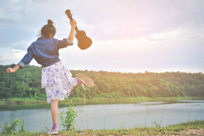 Full length rear view of young woman dancing with musical instrument by lake