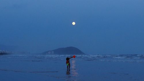 Children standing on beach against clear sky and moon