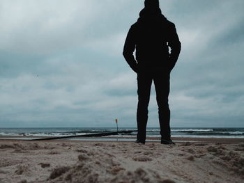 Rear view of silhouette man standing at beach against sky