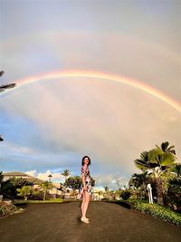 Full length of woman standing on road against rainbow in sky