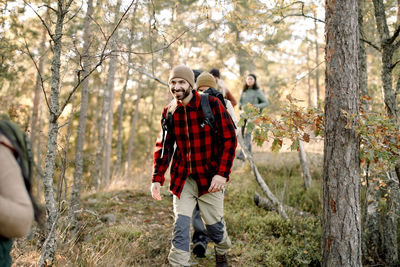 Smiling man hiking with friends amidst trees in forest