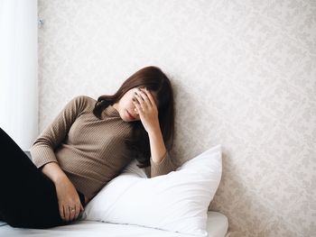 Woman with headache leaning on bed at home