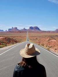 Rear view of woman wearing hat standing on road against sky