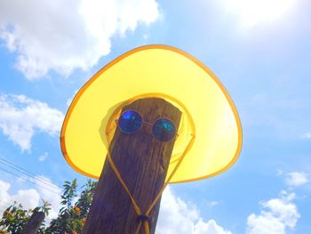 Low angle view of sunglasses with sun hat on wooden post against sky