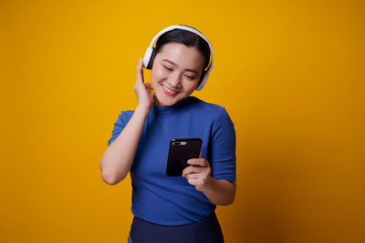 Portrait of smiling young man using mobile phone against yellow background