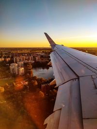 Cropped image of airplane flying over park in city against clear sky during sunset